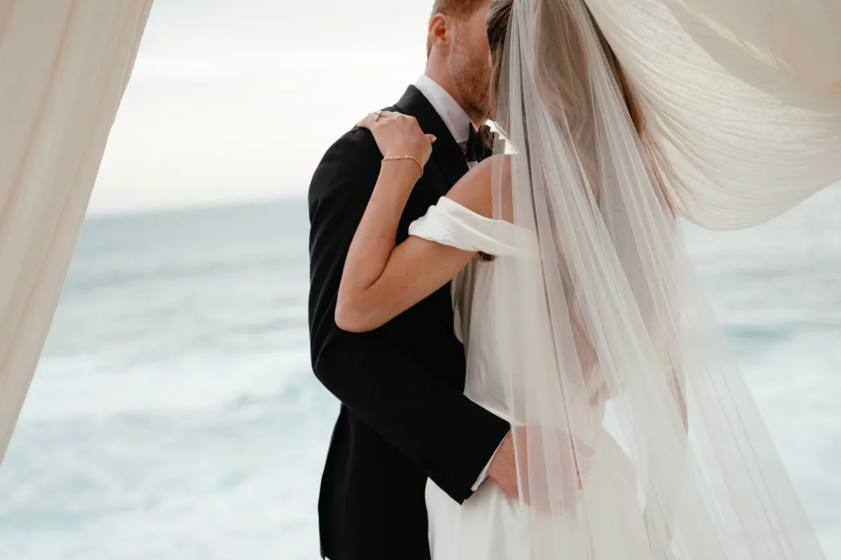 cabo wedding ceremony couple embrace engaging events ali chicago planner - Luxury Cabo Wedding at The Cape, a Thompson Hotel Luxury Cabo wedding ceremony moment with bride and groom embracing under draped ceremony arch at The Cape Thompson Hotel, planned by Chicago wedding planner Engaging Events by Ali