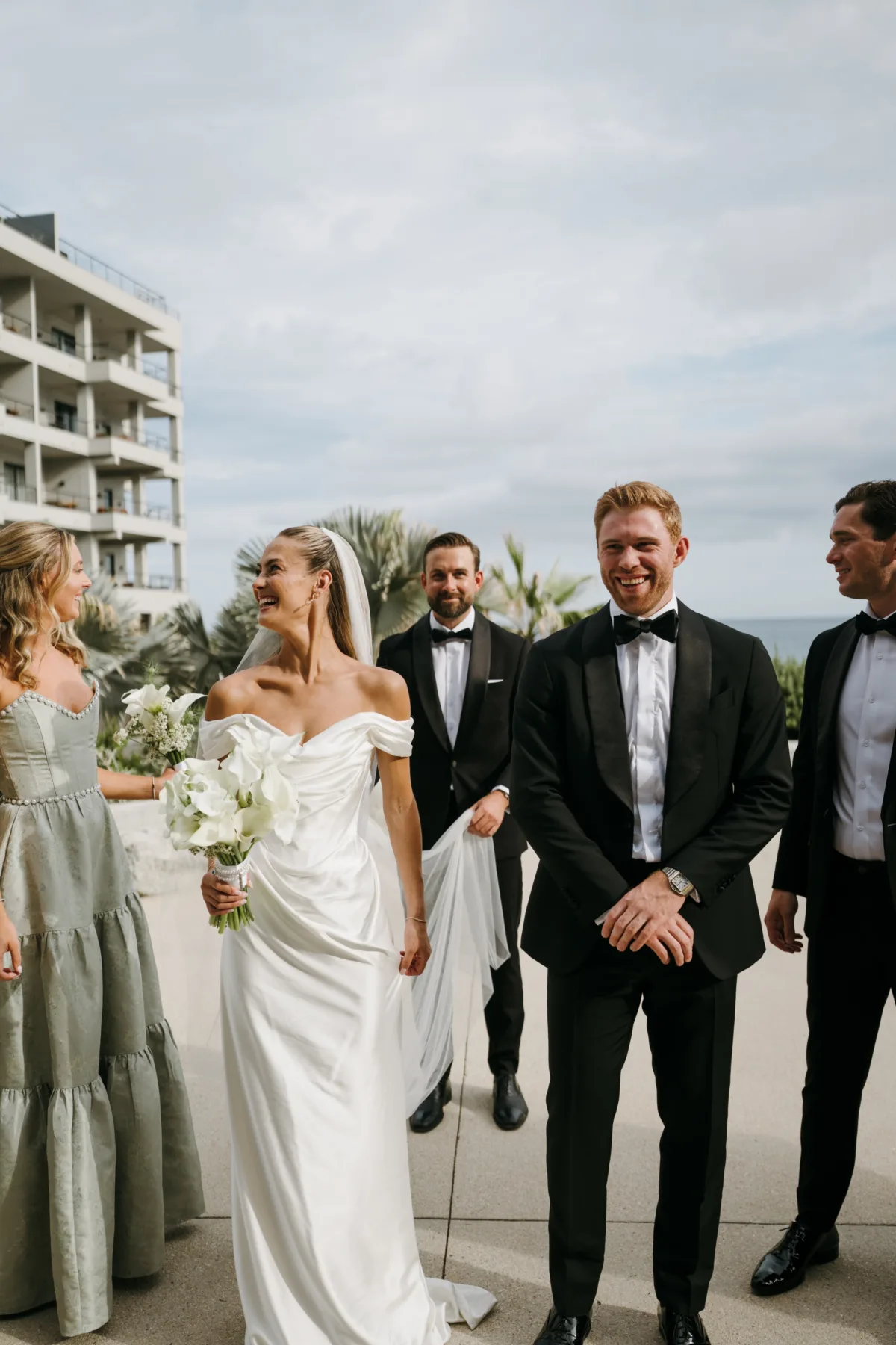 luxury cabo destination wedding party the cape thompson hotel - Luxury Cabo Wedding at The Cape, a Thompson Hotel Luxury destination wedding party walking at The Cape, a Thompson Hotel in Cabo San Lucas with bride in off-shoulder gown and groom in black tuxedo