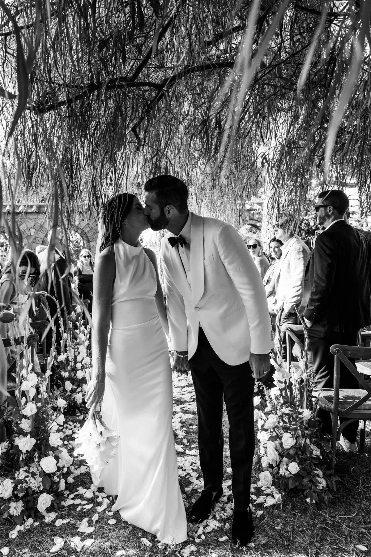 amalfi coast destination wedding ceremony kiss engaging events ali capo santa fortunata - An Effortless Amalfi Coast Celebration Bride and groom sharing first kiss during outdoor wedding ceremony under willow tree at Capo Santa Fortunata in Sorrento Italy planned by Engaging Events by Ali