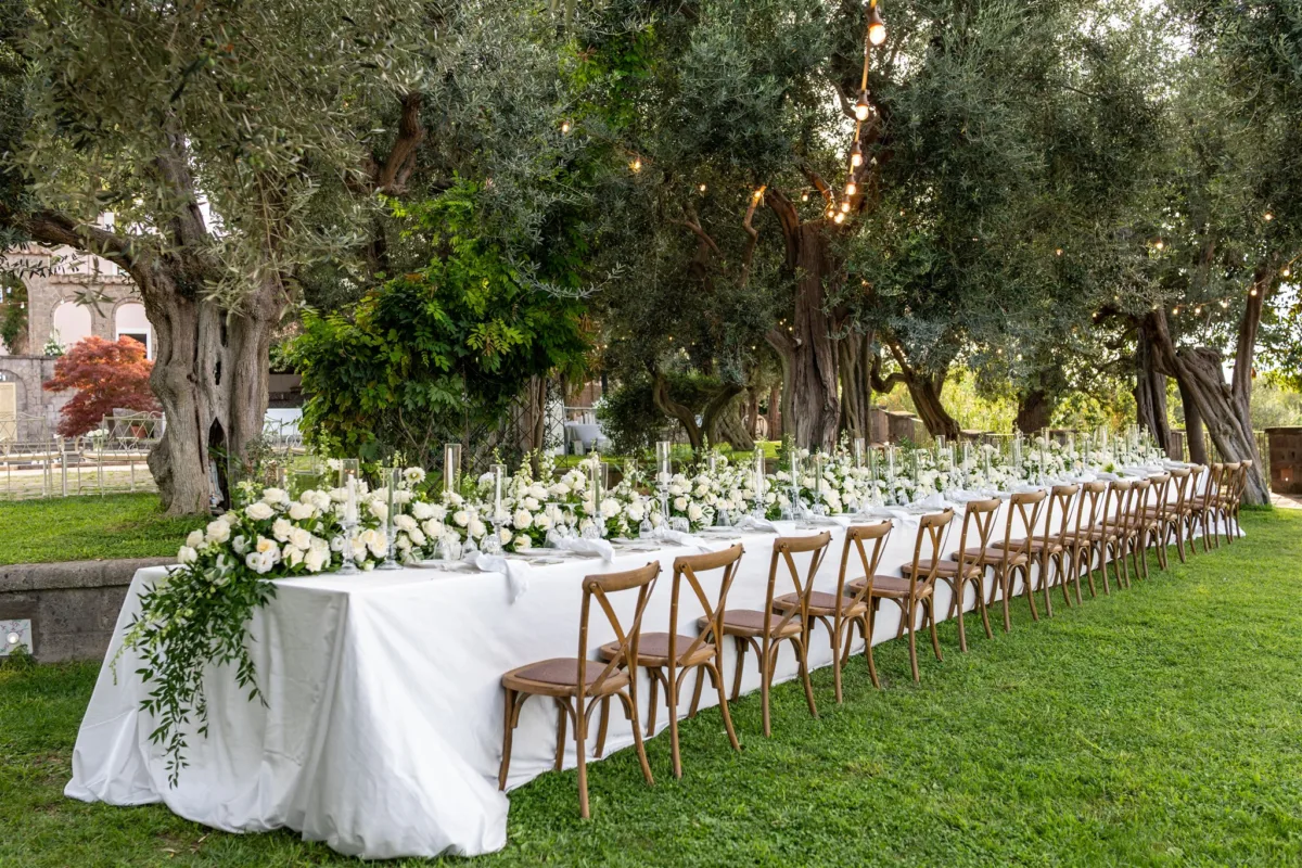 amalfi coast wedding planning engaging events ali capo santa fortunata outdoor reception - An Effortless Amalfi Coast Celebration Elegant outdoor wedding reception table setup under olive trees at Capo Santa Fortunata in Sorrento Italy planned by Engaging Events by Ali with white floral centerpieces and cross back chairs