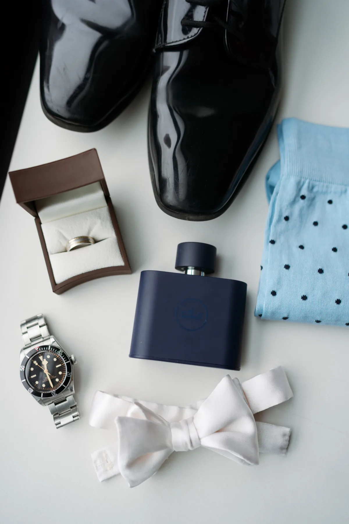 chicago groom wedding details ritz carlton engaging events - A Golden Ritz-Carlton Chicago Celebration Elegant groom's wedding day accessories including black patent leather shoes, silver watch, bow tie, wedding ring, cologne and polka dot socks arranged for Chicago Ritz-Carlton wedding planned by Engaging Events by Ali