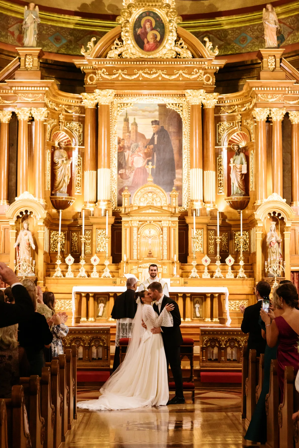 chicago wedding planning engaging events ali church ceremony kiss - A Golden Ritz-Carlton Chicago Celebration Bride and groom share first kiss during church wedding ceremony in ornate golden sanctuary, coordinated by Chicago wedding planner Engaging Events by Ali