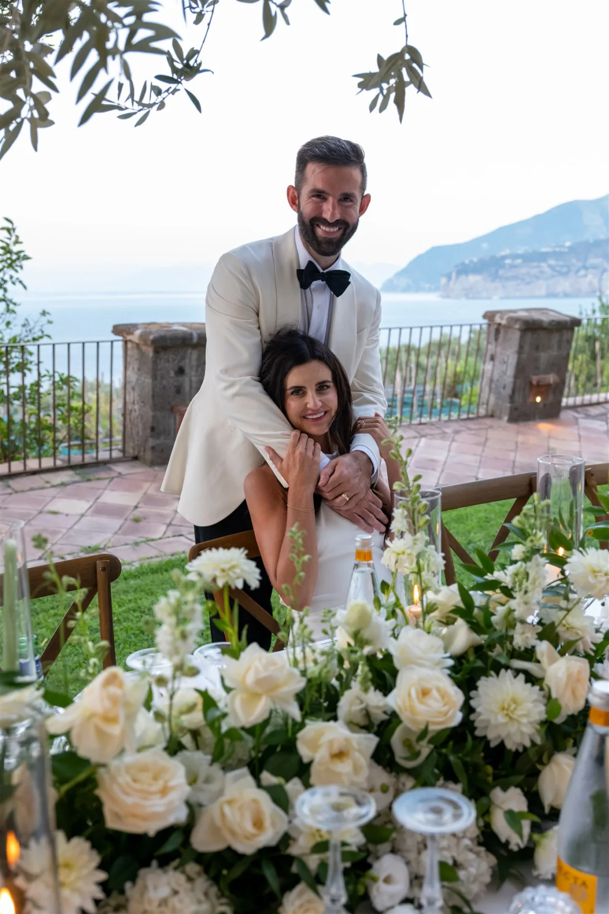 engaging events ali wedding planning sorrento italy capo santa fortunata - An Effortless Amalfi Coast Celebration Bride and groom embrace at romantic seaside reception with white floral centerpieces at Capo Santa Fortunata venue in Sorrento Italy planned by Engaging Events by Ali