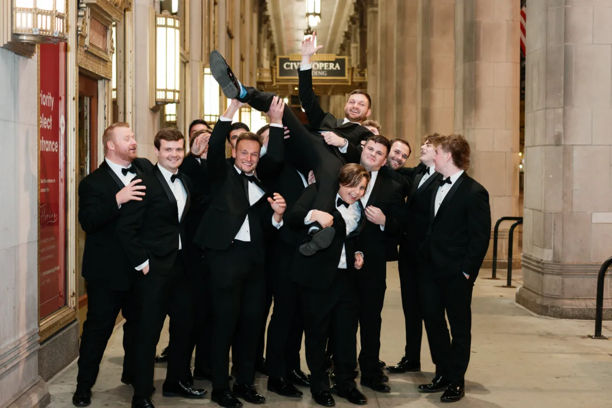 wedding planning engaging events ali groomsmen lyric opera chicago - A Golden Ritz-Carlton Chicago Celebration Groomsmen celebrating at Chicago wedding planned by Engaging Events by Ali with groom being lifted in formal tuxedos